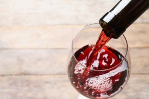 Pouring red wine from bottle into glass on blurred background, closeup.